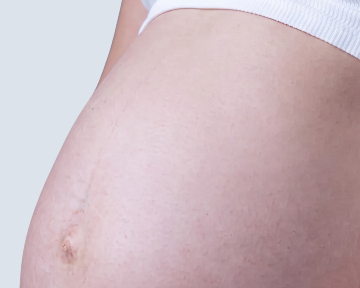 A pregnant woman’s bump, seen from the side, in a white top.