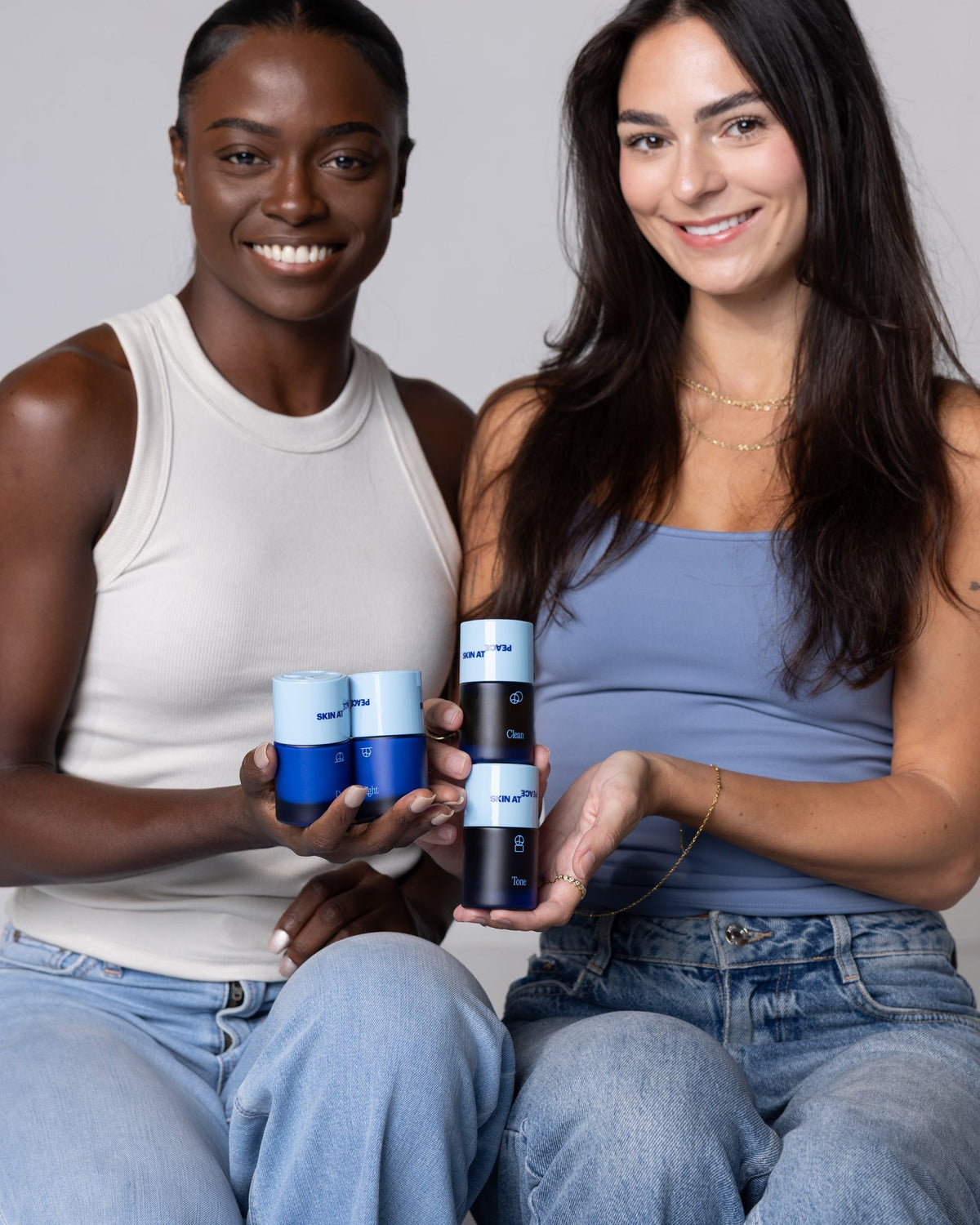 Two friends smiling, each holding Skin At Peace bottles.